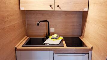 Eine kleine Küche mit Holzschränken, einem schwarzen Spülbecken und einem kleinen Kühlschrank.