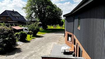 Ein Wohngebiet mit befestigter Auffahrt, einer Ziegelterrasse mit Gartenmöbeln und einem großen Baum im Hintergrund.