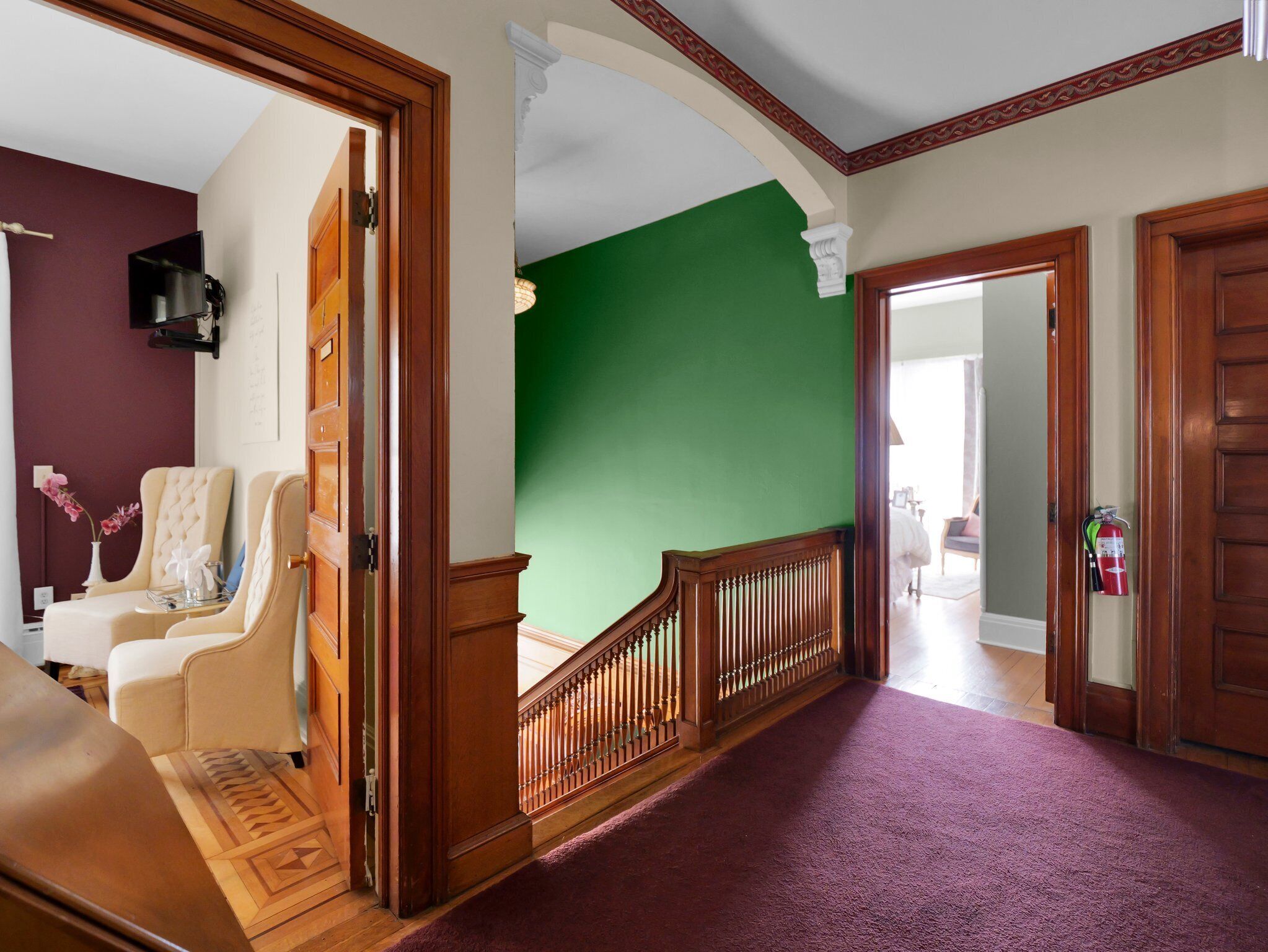 A hallway with a green wall, wooden doors, and a staircase with a wooden railing.