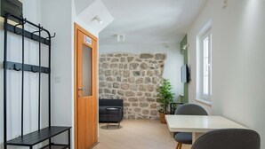A room with a stone wall, a wooden door, a black metal shelf, a small round table, and a grey chair. - Casa Campana (Kotor)