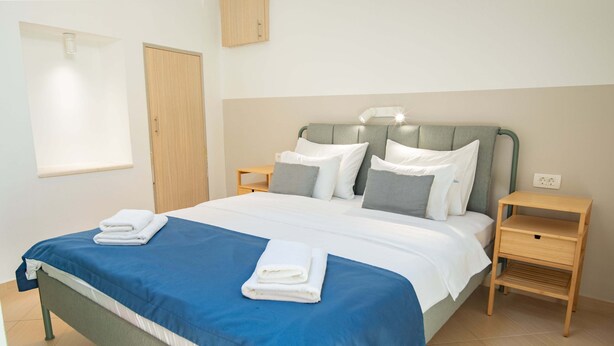 A neatly made bed with blue bedding and white pillows, a bedside table with a lamp, and a wooden nightstand with a drawer. - Casa Campana (Kotor)
