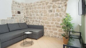 A living room with a stone wall, a grey sofa, a small round table, and a potted plant. - Casa Campana (Kotor)