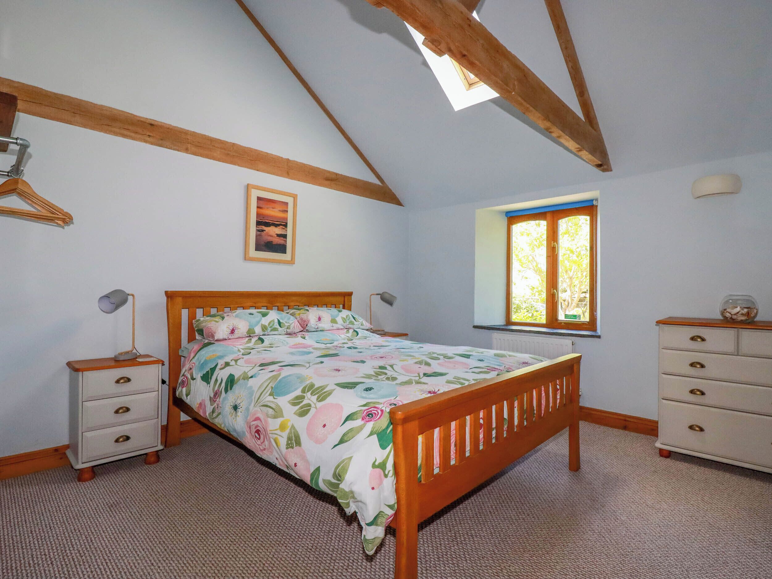 Un dormitorio con una cama de madera, una mesita de noche, un aparador, una ventana con contraventanas azules y un cuadro en la pared.