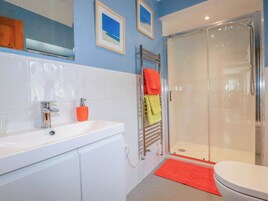 Un baño con un lavamanos blanco, cabina de ducha de vidrio y una alfombra de baño roja.