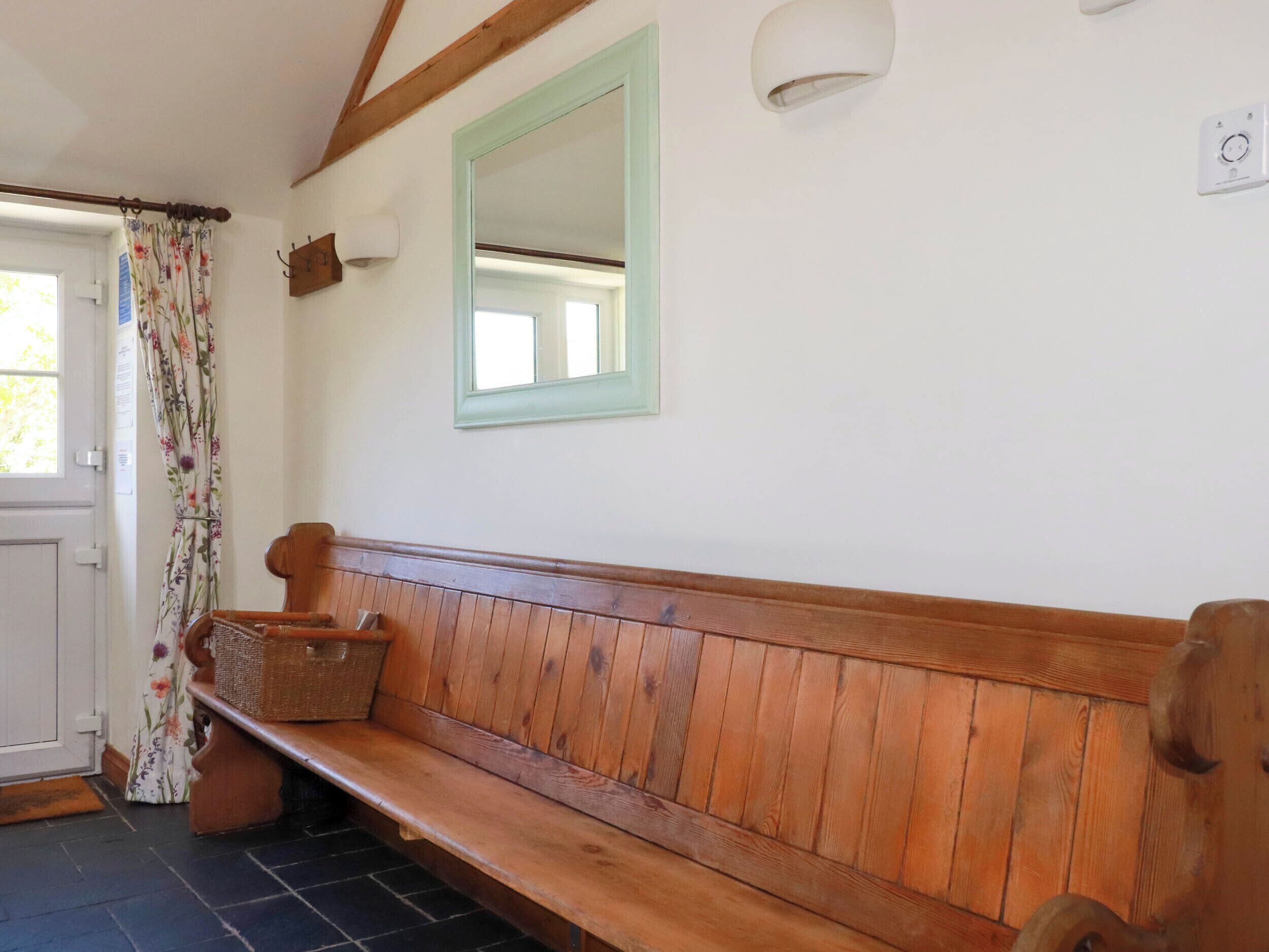 Un banco de madera en una habitación con una puerta, un espejo y un aplique de pared.