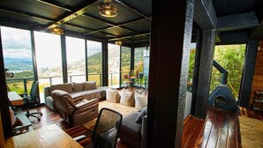 Una zona de estar acogedora con sofá, sillas y una mesa, ventanas amplias que ofrecen vistas al exterior y un estufa de leña.