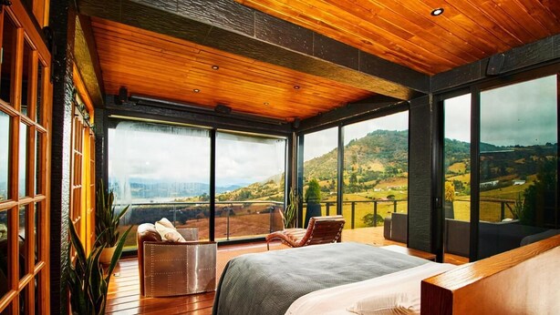 Un dormitorio amplio con una cama grande, suelo de madera y un balcón con vistas panorámicas.