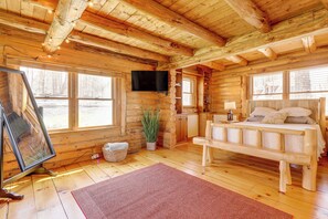 En stuga med träpanel på insidan, en säng av trä, en tv som hänger på väggen och ett stort fönster.