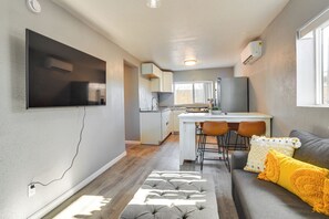 Una cucina moderna con TV a schermo piatto, un'area pranzo con uno sgabello da bar e un divano grigio con cuscini gialli.