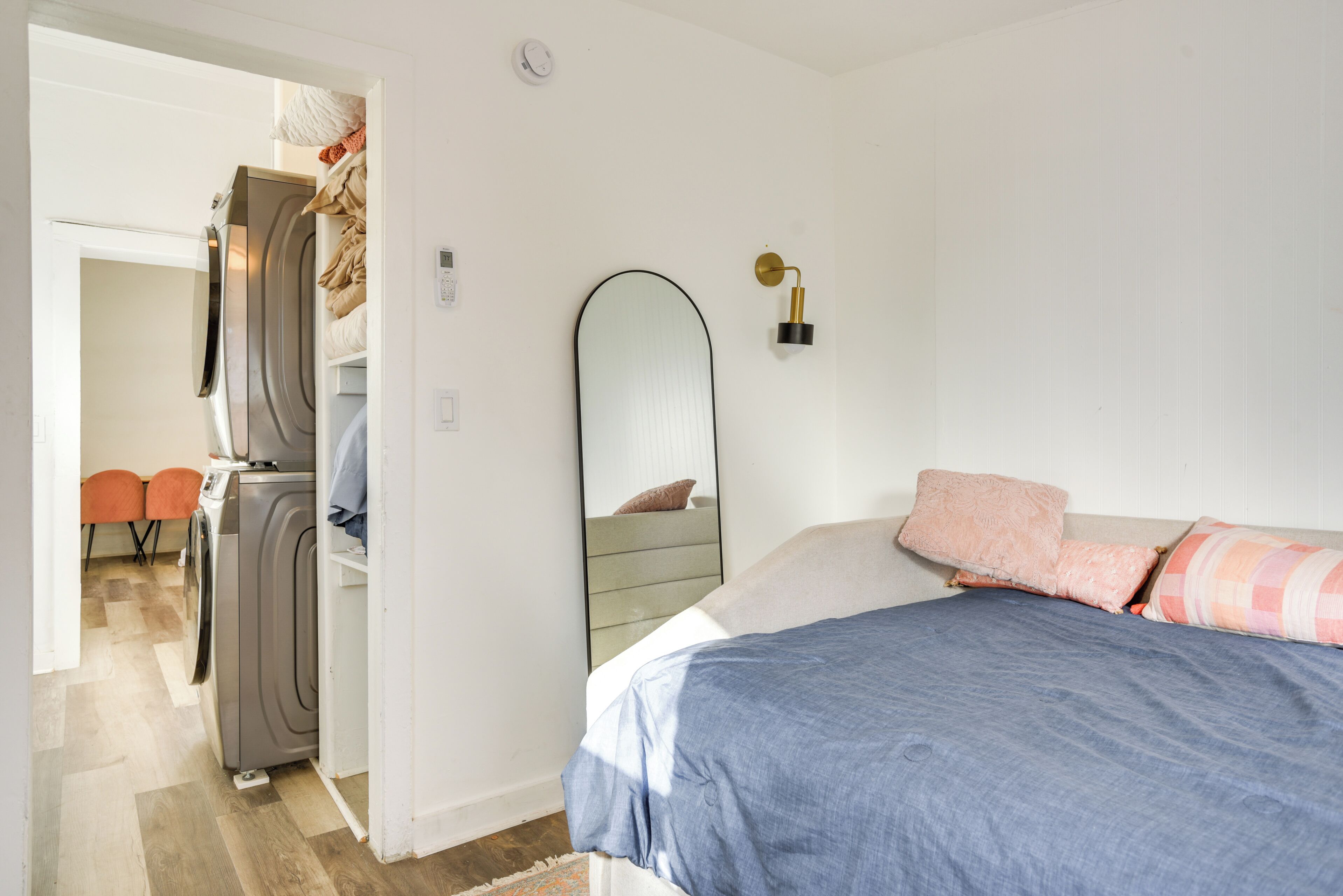 A bedroom with a bed, a mirror, and a washing machine in the adjacent room.