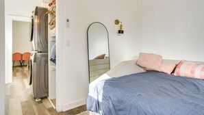 A bedroom with a bed, a mirror, and a washing machine in the adjacent room. - Near UNM & ABQ BioPark: East Dtwn Studio (Albuquerque)