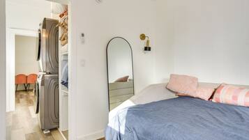 A bedroom with a bed, a mirror, and a washing machine in the adjacent room.