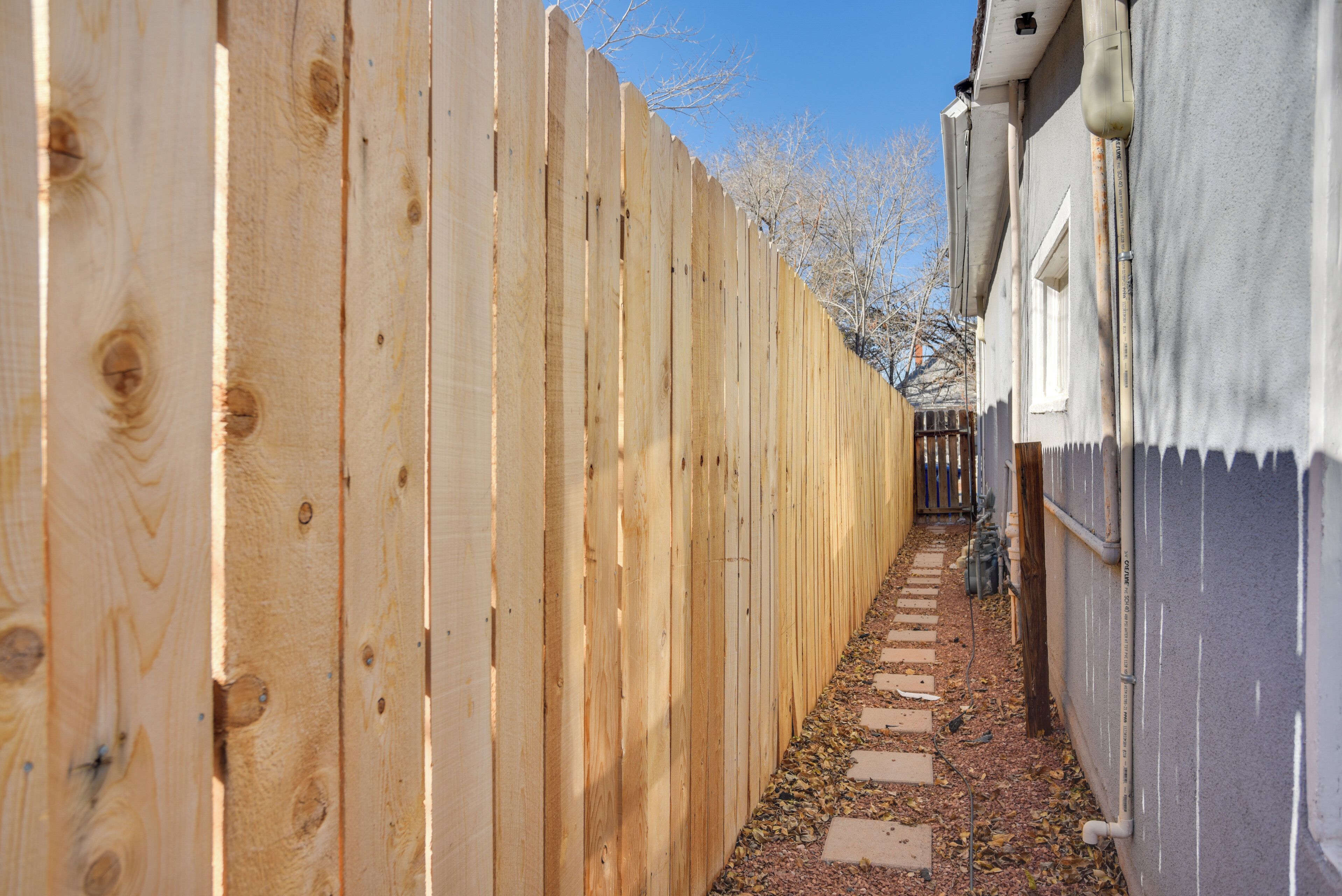 A narrow wooden fence-lined pathway leading to a building with a gray exterior and a window.