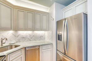 Una cocina con muebles blancos, un refrigerador de acero inoxidable y un salpicadero de azulejos tipo espiga.