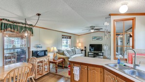A compact kitchen with wooden cabinets, a dining area with a wooden table and chairs, a microwave, and a television. - Waterfront Home w/ Boat Slips in Northern Michigan (Gladwin)