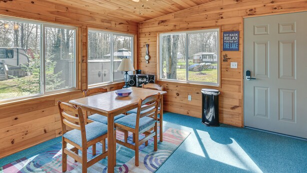 A wooden cabin interior with a dining table, chairs, a ceiling fan, and large windows overlooking a yard. - Waterfront Home w/ Boat Slips in Northern Michigan (Gladwin)