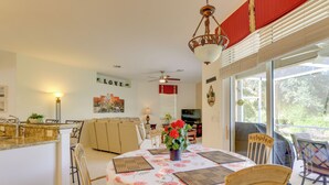Un coin repas avec une table dressée pour quatre personnes, entourée de chaises, un ventilateur de plafond et une vue dégagée sur l’extérieur grâce à de grandes fenêtres.