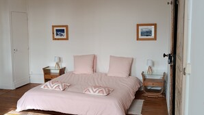 Un dormitorio con una cama, dos mesitas de noche, una puerta y dos cuadros en la pared.