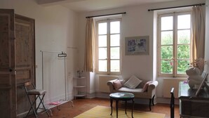 Una habitación con sofá, una mesita, un radiador, una ventana con cortinas, un perchero y una puerta.