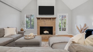 Una sala moderna con chimenea, sofás grises y un televisor de pantalla plana montado en la pared.