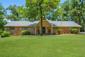A single-story brick house with a front porch, a lawn, and a large tree in the center. - CHAPEL HAVEN \\ 6 Bedrooms \\ 4 Bathroom \\ 8 Beds \\ 2-Unit Home \\  2 Kitchens (Tallahassee)