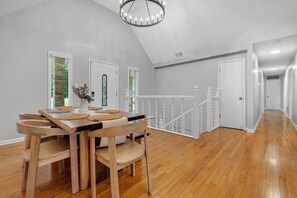 A dining area with a wooden table and chairs, a chandelier, and a staircase leading to another level.