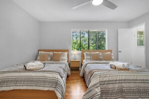 Un dormitorio con dos camas, un ventilador de techo, una ventana con persianas y una puerta.