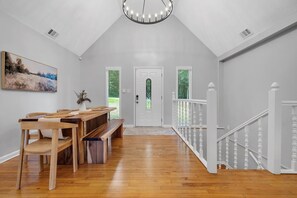 A spacious room with a wooden dining table, benches, and a staircase with white railings.