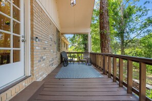 A covered outdoor area with a wooden deck, two Adirondack chairs, and a patterned rug.