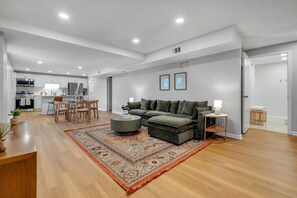 Una sala moderna con sofá, reposapiés y una mesita de centro, un comedor con sillas y una mesa, y una cocina con electrodomésticos.