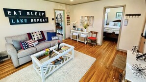 A living room with a grey sofa, a white coffee table, and a wooden floor. There is a sign on the wall that reads "EAT SLEEP LAKE REPEAT". - Coeur d' Lovely (Coeur d'Alene)