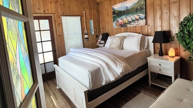 A cozy wooden cabin bedroom with a bed, nightstands, a heater, and a painting on the wall. - Coeur d' Lovely (Coeur d'Alene)