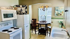 A compact kitchen with a stove, microwave, refrigerator, and sink. There is a dining table with chairs and a chandelier above. - Coeur d' Lovely (Coeur d'Alene)