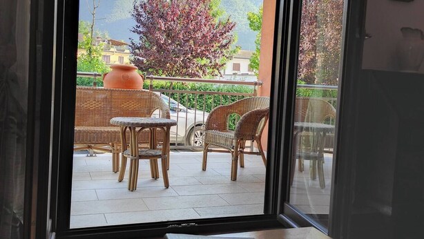 Une pièce dotée d’une porte-fenêtre coulissante donnant sur un patio extérieur aménagé avec des meubles en osier et un grand pot en terre cuite.