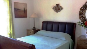 Une chambre à coucher avec un lit, une table de chevet, une lampe, une horloge murale et un tableau encadré.