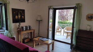Un salon comprenant un canapé, une table basse, un téléviseur, une lampe et un balcon aménagé avec du mobilier d’extérieur.