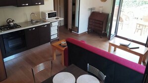 Une cuisine compacte équipée d’une cuisinière, d’un four à micro-ondes et d’un évier. On y trouve également un coin repas avec une table et des chaises, ainsi qu’un canapé. Une grande fenêtre offre une vue sur l’extérieur.