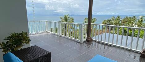A balcony with a blue cushioned lounge chair, a potted plant, and a view of the sea.