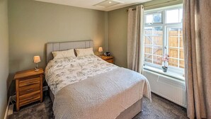Une chambre à coucher avec un lit, deux tables de chevet, une fenêtre avec des rideaux et une vue sur une clôture en bois.