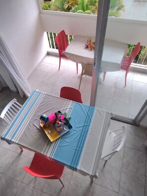 Un balcon avec une table à manger pour deux personnes, des chaises rouges et une vue sur le jardin.