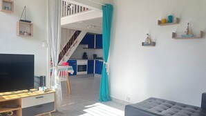 Ein modernes Wohnzimmer mit Fernseher, einer Couch und einer Küche im Hintergrund.