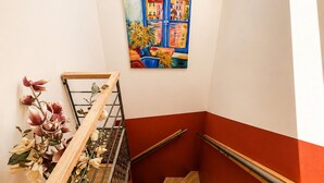 Een trap met houten treden en metalen leuningen, een aan de muur hangend schilderij en een plant met bloemen.