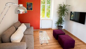 Een moderne woonkamer met een bank, een salontafel, een televisie en een raam met uitzicht op bomen.