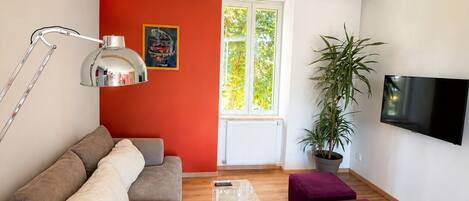 A modern living room with a sofa, a coffee table, a TV, and a window with a view of trees.