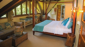 Een slaapkamer met een houten baldakijnbed, een bank, een eettafeltje en een raam met gordijnen.