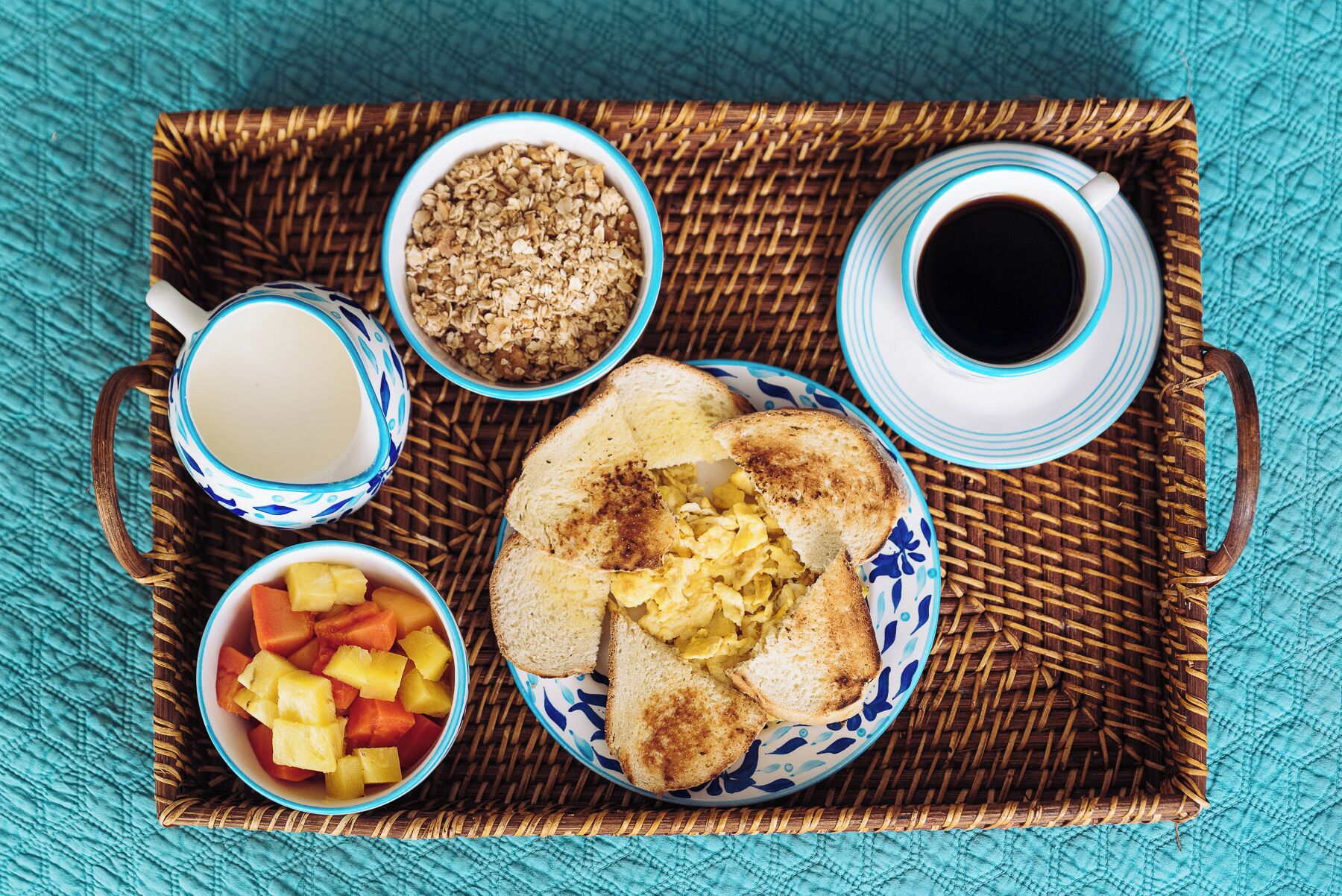 Una bandeja de desayuno con tostadas, huevos revueltos, fruta, granola y café.