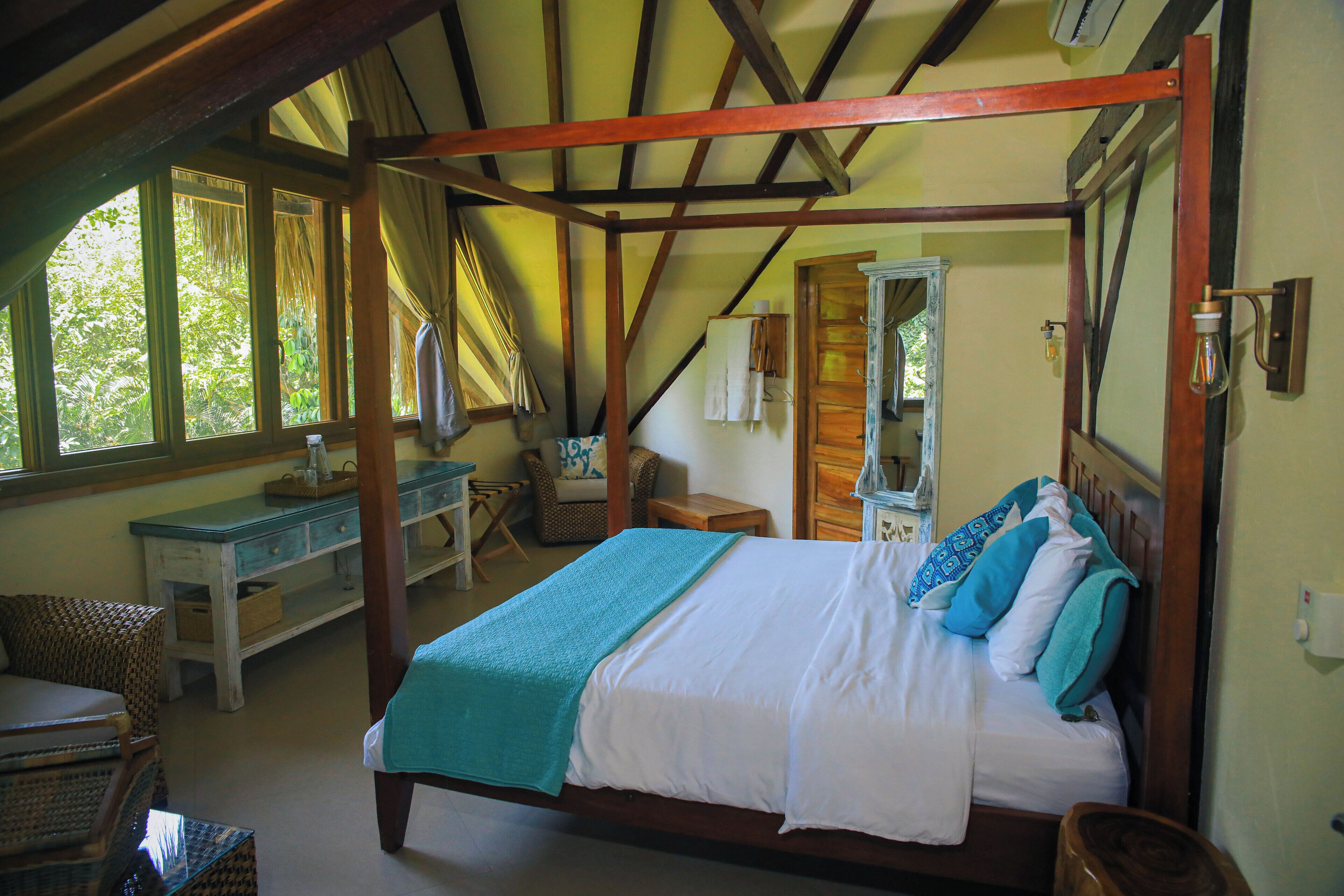 A four-poster bed with a wooden frame, a desk with a chair, and a window with curtains.