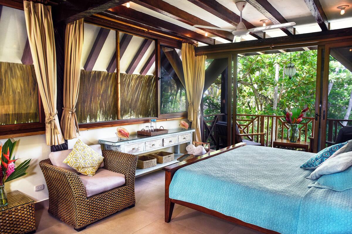 A bedroom with a bed, a sofa, a vanity, and a view of the outdoors.