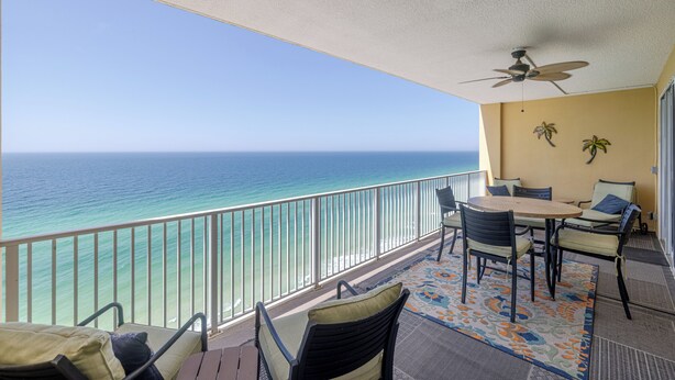 Un balcon avec vue sur l’océan, un ventilateur de plafond et une table avec des chaises.