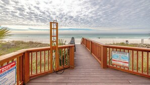 Une promenade en bois mène à une plage où un panneau avertit de la présence de courants de contre-rivage.